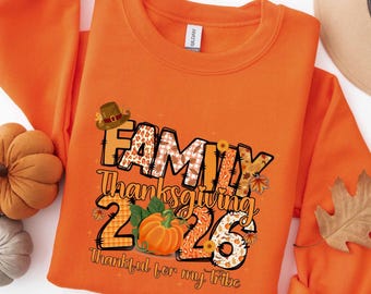 May include: An orange crewneck sweatshirt featuring a graphic print with the text "FAMILY Thanksgiving 2026" and "Thankful for my tribe". The design includes a brown pilgrim hat, a pumpkin, and various autumn-themed patterns like plaid and leopard.