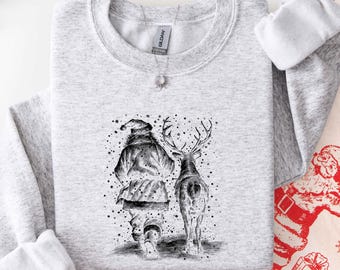 May include: A light gray crewneck sweatshirt featuring a black and white ink-style illustration of Santa Claus and a reindeer walking away from the viewer, surrounded by scattered dots, with a Gildan brand tag visible at the neckline.