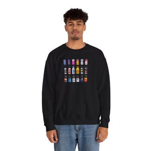 May include: Black sweatshirt featuring a grid of colorful, miniature beverage cans. The cans display various designs and colors, including blue, pink, yellow, and red. The sweatshirt is a casual, long-sleeved garment.