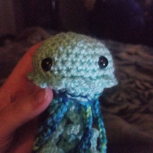 May include: A crocheted jellyfish toy with a light blue body and long blue, green, and white tentacles. The jellyfish has black button eyes.