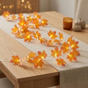 May include: A string of LED lights featuring artificial maple leaves in shades of orange, yellow, and red. The leaves are arranged along a thin, flexible wire, with small warm white lights positioned behind each leaf to create a glowing effect.