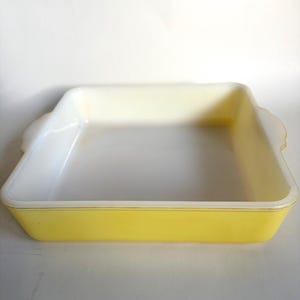 Peut inclure: Un plat de cuisson carré en verre opaque avec un extérieur jaune vif et un intérieur blanc lisse. Le plat présente des poignées intégrées sur deux côtés opposés, un fond plat et des parois droites légèrement inclinées pour la cuisson.