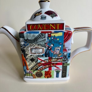 May include: A square white ceramic teapot featuring a colorful collage of Covent Garden imagery. The lid displays a palette, fan, and cup, with the text COVENT in a red box. The body shows street performers, flowers, and the text COVENT GARDEN MARKET.