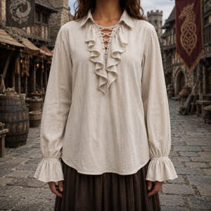 Peut inclure: Une chemise beige à manches longues dotée d'un laçage sur le devant, d'un col et de volants verticaux le long de l'encolure. Le vêtement présente des manches longues terminées par des poignets évasés et volantés, offrant un aspect texturé.
