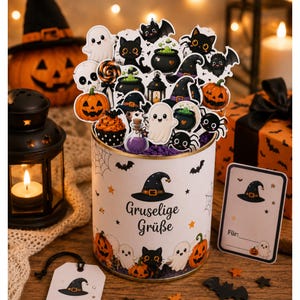 May include: A cylindrical white gift container decorated with Halloween motifs and the German text Gruselige Grüße. It is filled with various die-cut paper toppers featuring ghosts, black cats, pumpkins, spiders, and cauldrons, plus a matching gift tag.