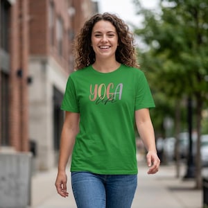 May include: A bright green short-sleeved t-shirt featuring the text "YOGA life" printed on the chest. The word "YOGA" is written in a multi-colored gradient font, while the word "life" is written in a black cursive script font.