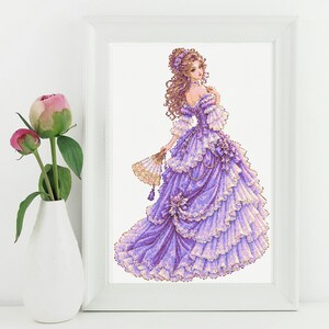 May include: A framed print featuring an illustration of a person with long curly brown hair wearing a voluminous, multi-layered lavender and white ball gown with lace details, holding a small decorative fan in a right hand.