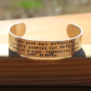 May include: A silver metal bracelet with an engraved quote: "Know your own happiness. You want nothing but patience - or give it a more fascinating name - call it hope."