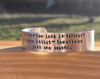 May include: A silver metal bracelet with the quote "Alice - How long is forever? White Rabbit - Sometimes Just one second." engraved on it.