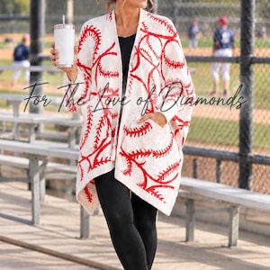 May include: An open-front cream cardigan featuring a red baseball stitch pattern, long sleeves, and two front pockets. The garment is worn over a black top and black leggings, paired with white sneakers. The text "For The Love of Diamonds" is visible.