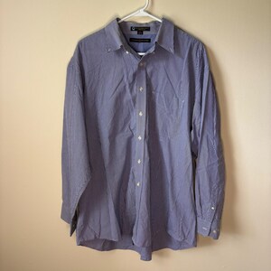 May include: A long-sleeve button-down shirt featuring a fine blue and white micro-check pattern. The shirt includes a pointed collar, a front button placket, and a single chest pocket. The interior neck label displays the Tommy Hilfiger brand name.