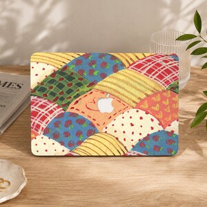 Può includere: Una skin per laptop con un design a patchwork colorato che presenta vari motivi, tra cui ciliegie rosse su sfondo blu, tartan verde, strisce gialle, quadrati a scacchi rossi e bianchi e crema con puntini rossi, con il logo Apple al centro.
