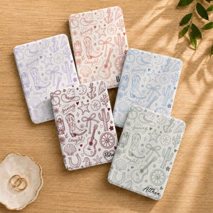 May include: Five rectangular notebooks with white covers featuring a repeating pattern of line drawings including cowboy boots, guitars, cacti, anchors, and shells. Each notebook displays the word sunny and a unique name like Flora or Althea.