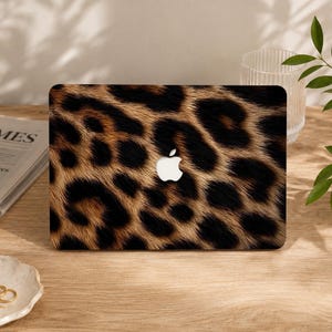 May include: A laptop skin featuring a realistic brown, tan, and black leopard print pattern. The design covers the entire rectangular surface of the laptop lid, with a central cutout revealing the white Apple logo in the middle of the print.