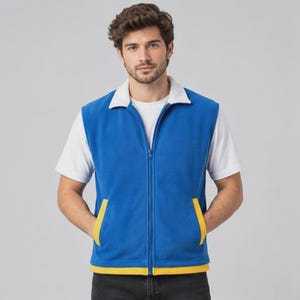 Könnte beinhalten: Eine leuchtend blaue Fleeceweste mit weißem Umlegekragen, durchgehendem Frontreißverschluss und zwei Vordertaschen mit gelber Einfassung. Der untere Saum der Weste ist ebenfalls mit einem gelben Band versehen, getragen über einem schlichten weißen T-Shirt.