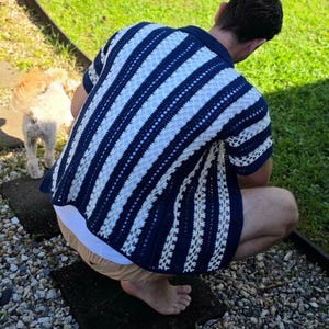 Peut inclure: Une chemise à manches courtes boutonnée avec un motif à rayures verticales bleu marine et blanc. Le vêtement est fabriqué avec un design en maille crochetée ajourée, présentant des rayures bleu marine alternées et des panneaux en dentelle blanche.