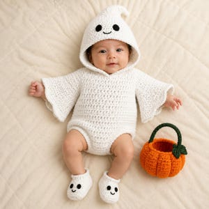 Op de afbeelding: Een wit gehaakt spookkostuum bestaande uit een romper met capuchon, uitlopende mouwen en bijpassende slofjes, elk met zwarte garen ogen en een geborduurde mond. Naast de outfit staat een klein, rond, oranje gehaakt pompoenmandje met groen hengsel.