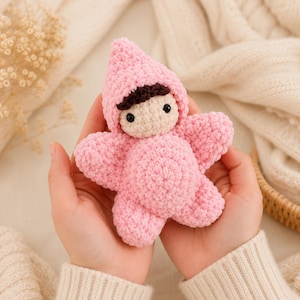 Peut inclure: Une petite poupée crochetée à la main avec un corps rose en forme d'étoile et une capuche pointue assortie. La poupée présente un visage couleur crème, des cheveux brun foncé et deux petits yeux en perles noires, en fil pelucheux.