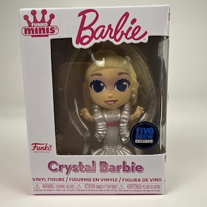 May include: A Funko Minis Crystal Barbie vinyl figure inside a white cardboard display box. The figure has blonde hair, large blue eyes, and wears a silver dress with a pink waist accent. The box features the text Funko Minis, Barbie, and Five Below Exclusive.