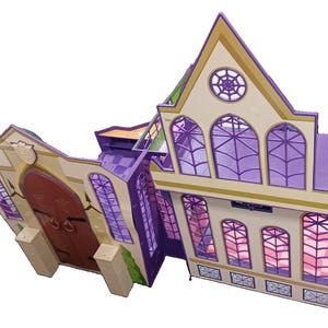 Può includere: Una casa delle bambole in plastica a più livelli con esterno color crema, finiture e dettagli viola. La struttura presenta finestre ad arco con vetri viola a ragnatela, una grande porta doppia marrone e una sezione con tetto a punta.