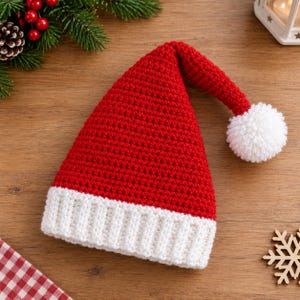 Könnte beinhalten: Eine rote, gehäkelte Weihnachtsmütze mit weißem Rippenbündchen und einem weißen Bommel an der Spitze. Die Mütze ist in einem dichten Maschenmuster gefertigt und hat eine spitz zulaufende, leicht gebogene Form im klassischen festlichen Design.