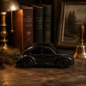 Peut inclure: Un modèle réduit de voiture classique en céramique noire brillante, doté d'une surface lisse et réfléchissante, d'ailes incurvées et de roues circulaires, positionné horizontalement pour montrer sa silhouette emblématique et son design compact.