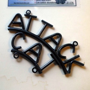 May include: Black metal sign spelling "ATTACK CAT" with a decorative cat illustration. The sign is made of wrought iron and includes the text "Wrought Iron Signs" and the Bevel Crafters logo.