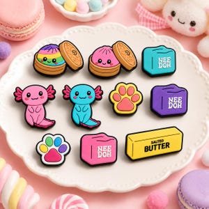 May include: A collection of colorful silicone charms featuring two rainbow and pink dumplings in bamboo steamers, two axolotls, two paw prints, three Nee Doh cubes in teal, purple, and pink, and a yellow rectangular salted butter block.