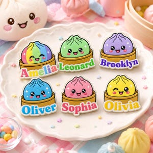 May include: Six enamel pins shaped like cartoon dumplings in bamboo steamers, each featuring a different color and name: Amelia in rainbow, Leonard in green, Brooklyn in purple, Oliver in blue, Sophia in pink, and Olivia in yellow.