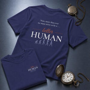 May include: A navy blue short-sleeved t-shirt featuring the text "Now, more than ever we must strive to be a... better HUMAN" in white and orange, accompanied by a small evolutionary graphic. A smaller version of the same design is on a folded shirt.