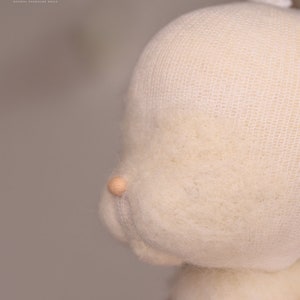 May include: Close-up of a white wool doll head with a mesh covering. The doll's nose is made of wood and is visible.