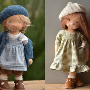 May include: Two handmade cloth dolls wearing dresses and hats. The doll on the left is wearing a blue and white plaid dress, a blue cardigan, and a blue beret. The doll on the right is wearing a green and white plaid dress, a beige beret, and is holding a small stuffed mouse.