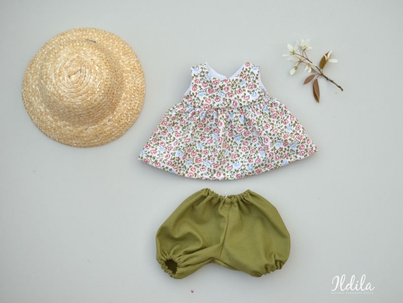 May include: A doll outfit set with a floral print dress, green bloomers, and a straw hat.