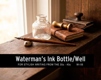May include: A vintage writing set including a clear glass Waterman's ink bottle, a wooden dip pen, a small stone pen rest, a leather-bound journal, and a wooden blotter. The set is displayed on a dark wooden surface.