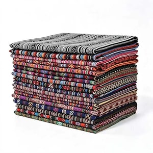 May include: A tall stack of folded fabric pieces, each featuring distinct patterns and color palettes. The top layer is black and white with geometric stripes, while the layers below display a variety of multicolored woven designs.