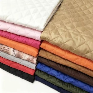 May include: A stack of folded quilted fabric pieces in various solid colors including white, pink, magenta, orange, tan, brown, blue, green, and black, along with one piece featuring a printed pattern of text and illustrations.