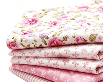 May include: A stack of five folded fabric pieces featuring various pink and white patterns. The top layer displays a floral print with pink roses and green leaves, followed by three layers of small pink floral motifs, and a bottom layer with pink stripes.