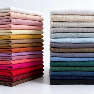 May include: Two tall, neat stacks of folded fabric squares arranged side by side. The left stack features warm tones including white, cream, pink, yellow, orange, and red. The right stack displays cool tones like white, gray, blue, green, and black.