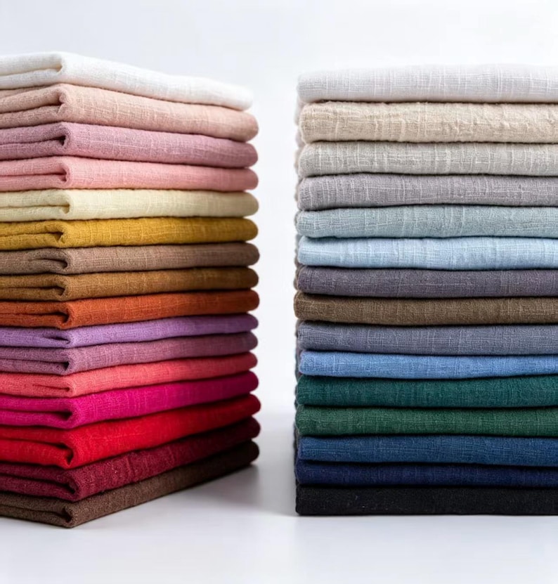 May include: Two tall, neat stacks of folded fabric squares arranged side by side. The left stack features warm tones including white, cream, pink, yellow, orange, and red. The right stack displays cool tones like white, gray, blue, green, and black.