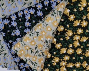 以下が含まれることがあります： 刺繍された花柄の4枚の布地。2枚は黒地に青または黄色の花、もう2枚は明るいベージュ地に青または黄色の花が描かれています。花には白い中心部と濃い緑色の茎があります。