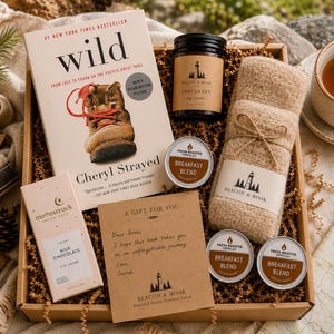May include: A gift box containing the book Wild by Cheryl Strayed, a Beacon & Book vanilla candle, a pair of beige fuzzy socks, a Moonstruck milk chocolate bar, three small tins of Breakfast Blend coffee, and a handwritten gift note for Anna.