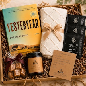 May include: A gift box containing a copy of the novel Yesteryear by Caro Claire Burke, a cream-colored knit blanket tied with a tan ribbon, three black Rishi Earl Grey tea packets, a jar of Beacon & Book candle, caramels, and a handwritten note.