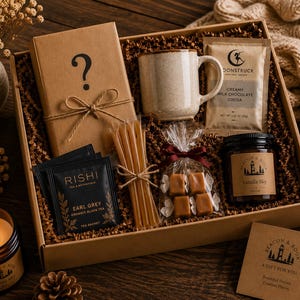 May include: A gift box containing a book wrapped in brown paper with a question mark, a speckled ceramic mug, a packet of Moonstruck creamy milk chocolate cocoa, Rishi Earl Grey tea sachets, honey sticks, caramels, and a Vanilla Sky candle.