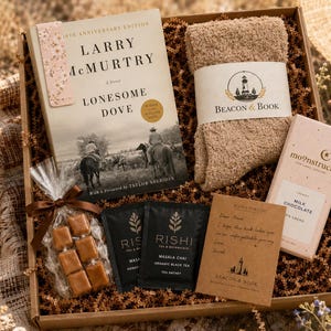 May include: A gift box containing a Lonesome Dove novel, a pair of beige fuzzy socks with a Beacon & Book label, a Moonstruck milk chocolate bar, two Rishi Masala Chai tea sachets, a small bag of caramels with a brown ribbon, and a note card.