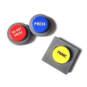 Puede incluir: Tres botones circulares y cuadrados con bases grises. Un botón circular rojo tiene el texto DO NOT PRESS en blanco. Un botón circular azul tiene el texto PRESS en blanco. Un botón cuadrado amarillo tiene el texto PANIC en negro.