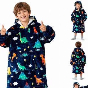 May include: A navy blue oversized hooded sweatshirt featuring a colourful dinosaur pattern with green, orange, and yellow dinosaurs, white clouds, and a large front pocket. The interior is lined with white fleece, and the sleeves have ribbed cuffs.