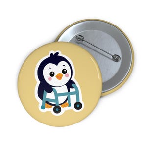 May include: A round pin-back button featuring a cartoon penguin with black and white feathers, orange feet, and a beak, standing while holding a blue mobility walker. The background of the button is a solid light yellow color with a metallic back.