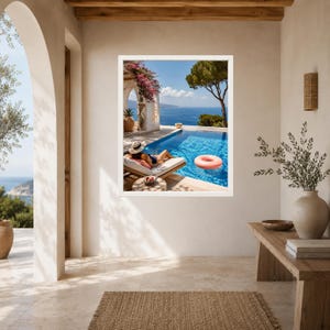 May include: A framed wall art print depicting a sunny Mediterranean terrace with a swimming pool, a person lounging on a sunbed, a pink inflatable ring floating in the water, vibrant pink bougainvillea flowers, and a distant blue sea view.
