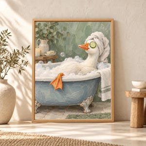 Framed funny duck bathroom wall art showing a white duck relaxing in a blue clawfoot bubble bath with cucumber slices over its eyes and a towel turban in a soft sage green bathroom.