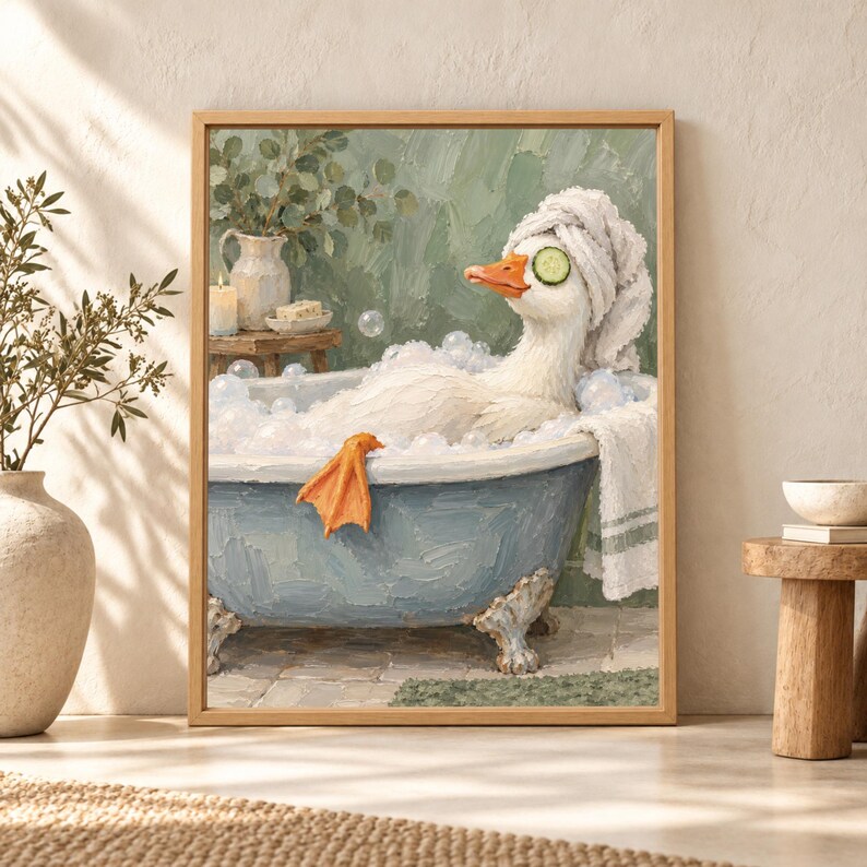 Framed funny duck bathroom wall art showing a white duck relaxing in a blue clawfoot bubble bath with cucumber slices over its eyes and a towel turban in a soft sage green bathroom.
